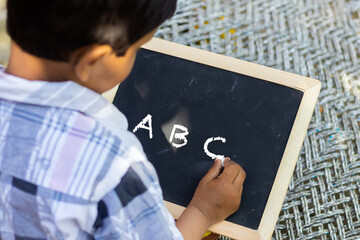little kid writing ABC on black slate pencil board