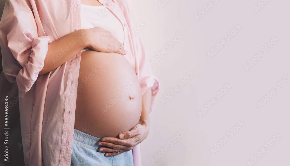 Wall mural Closeup beautiful pregnant woman belly with her hands. Pregnancy, maternity, preparation and expectation concept.