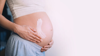 Pregnant woman applying moisturizer cream on her belly. Body skin care during pregnancy.