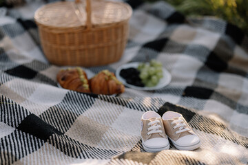 The concept of pregnancy and expecting a baby, maternity. Boy's shoes on basket with fruit and croissants in outdoor.