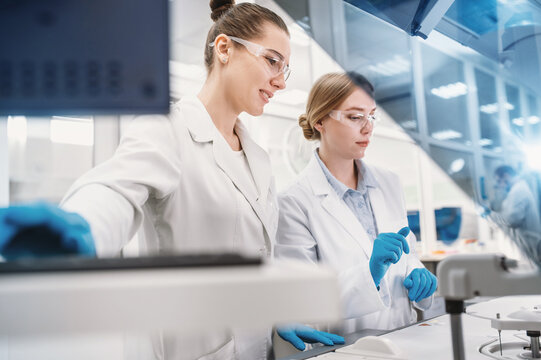 A team of laboratory technicians conduct a series of tests on a chemical analyzer in a biological laboratory. Two female scientists work in a modern equipped computer laboratory