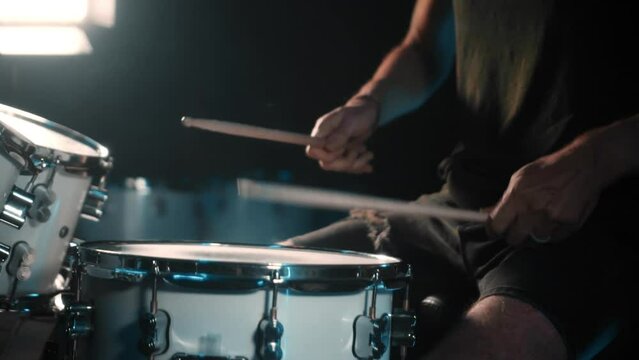 The drummer plays drums in a dark studio with lights on the back.