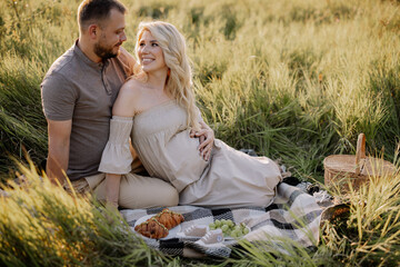 Beautiful pregnant couple in love spending time together in nature at sunset, having a picnic.