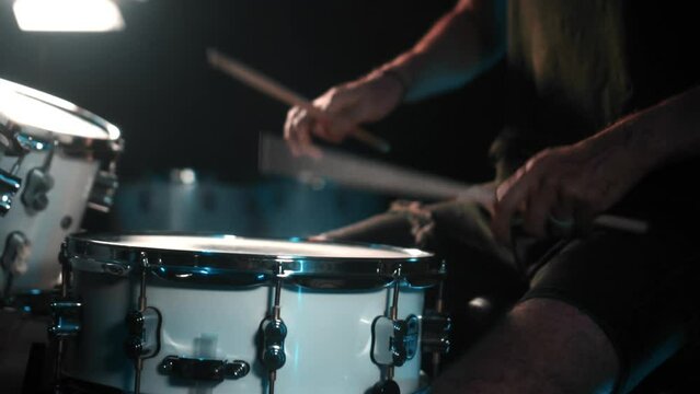 The drummer plays drums in a dark studio with lights on the back.