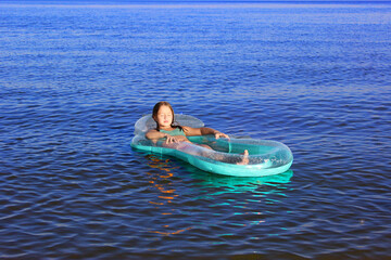 little happy girl in the sea with blond hair in a swimsuit floating in the sea on an inflatable...
