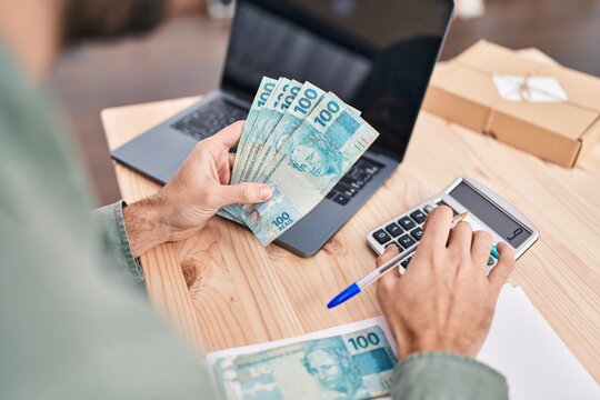 Young man ecommerce business worker holding brazil real banknotes accounting at office