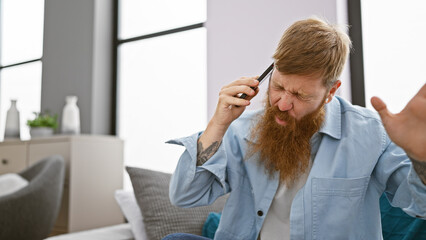 Unhappy young redhead man, argument escalating while using phone on sofa, expression shows...