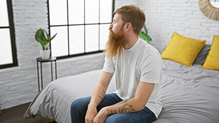 Handsome, young redhead man comfortably sitting on his bed in a relaxed morning, intentionally...