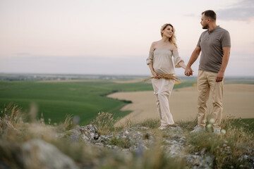 Portrait of a happy pregnant couple with a bouquet of sunflowers spending time together walking in the mountains at sunset