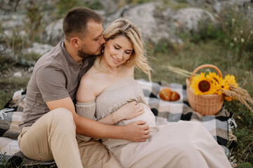 Beautiful pregnant couple in love spending time together in nature at sunset, having a picnic.
