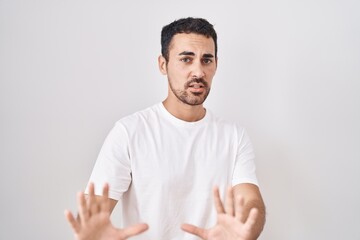 Handsome hispanic man standing over white background afraid and terrified with fear expression stop gesture with hands, shouting in shock. panic concept.