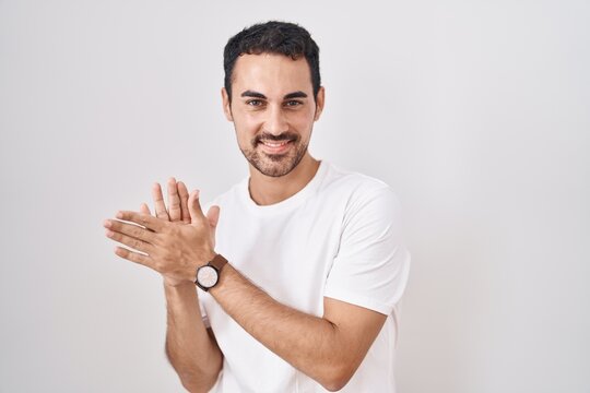 Handsome hispanic man standing over white background clapping and applauding happy and joyful, smiling proud hands together