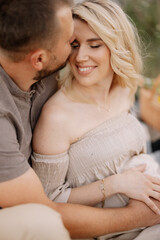 Beautiful pregnant couple in love spending time together in nature at sunset, having a picnic.