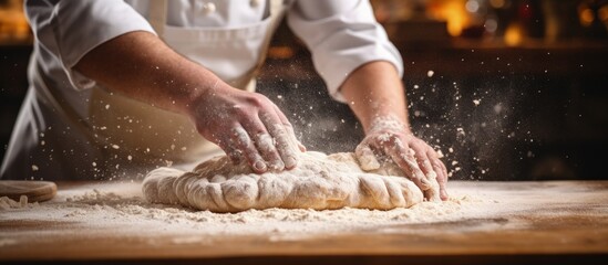 Close up of artisan baker sprinkling flour on fresh dough in rustic bakery kitchen Copy space image...