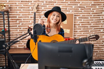 Fototapeta na wymiar Young caucasian woman playing classic guitar at music studio smiling happy pointing with hand and finger to the side