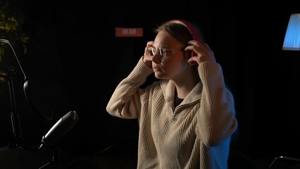 Beautiful young female dj speaks into microphone, records podcast or night news show for radio. Close up of podcast presenter or DJ talking on the microphone. Wears professional headphones