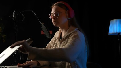 Beautiful young female dj speaks into microphone, records podcast or night news show for radio. Close up of podcast presenter or DJ talking on the microphone. Wears professional headphones