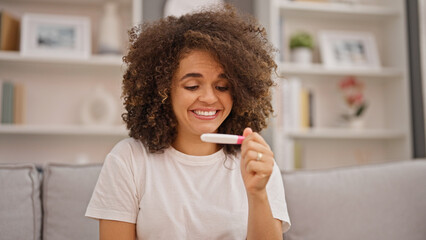 Young beautiful hispanic woman looking pregnancy test smiling at home