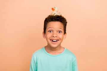 Photo of positive cheerful boy wear stylish clothes yellow duck on his head isolated over beige color background