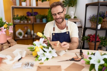 Middle age man florist holding letter and bouquet of flowers at flower shop