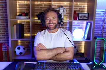 Middle age man with beard playing video games wearing headphones happy face smiling with crossed arms looking at the camera. positive person.