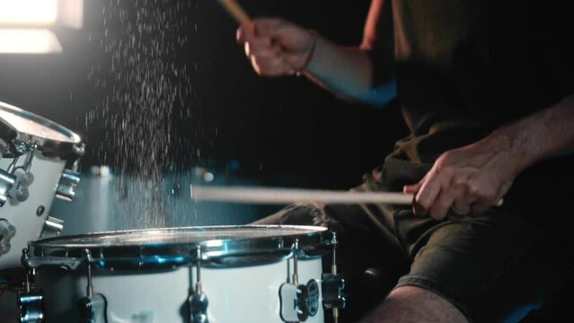 The drummer plays drums in a dark studio with lights on the back.