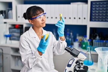 Young beautiful hispanic woman scientist holding lemon and test tube at laboratory