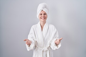 Blonde caucasian woman wearing bathrobe smiling cheerful offering hands giving assistance and acceptance.