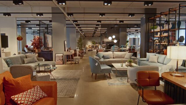 Dolly shot of big furniture store filled with variable couches, armchairs, coffee tables, houseplant pots and paintings