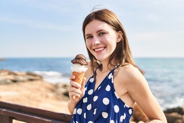 Young blonde woman tourist smiling confident holding ice cream at seaside