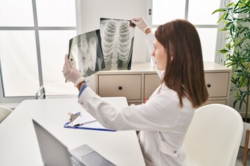 Young blonde woman doctor looking xray sitting on table at clinic