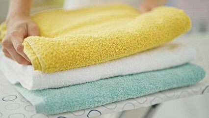 Young blonde woman folding towels at laundry room