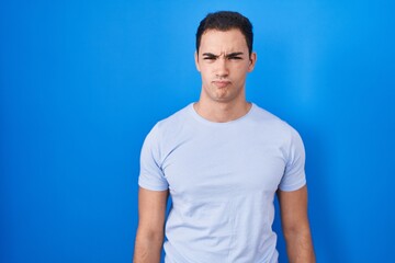 Young hispanic man standing over blue background skeptic and nervous, frowning upset because of problem. negative person.