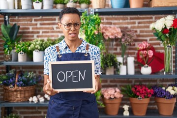 African american woman working at florist holding open sign clueless and confused expression. doubt...