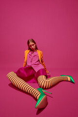 Extraordinary fashion. Full-length portrait of expressive young girl, lady in unusual, variegated orange striped tights, long skirt and short jacket.