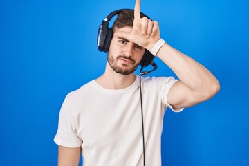 Hispanic man with beard listening to music wearing headphones making fun of people with fingers on...