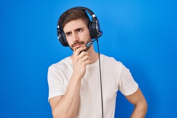 Hispanic man with beard listening to music wearing headphones with hand on chin thinking about...