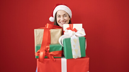 Young caucasian woman wearing christmas hat holding gifts over isolated red background