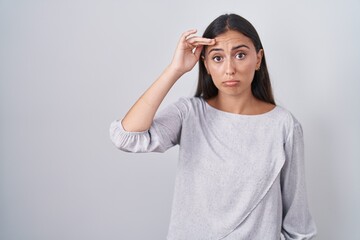 Young hispanic woman standing over white background worried and stressed about a problem with hand on forehead, nervous and anxious for crisis