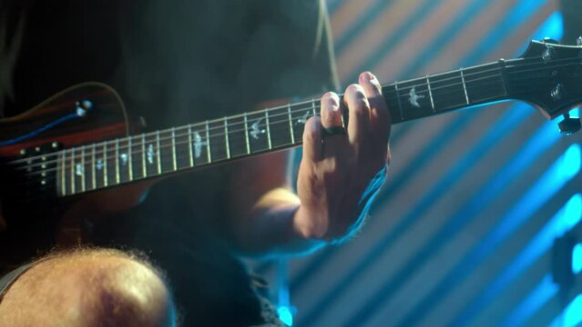 The young musician's hands play electro guitar in a dark studio with a light at the back