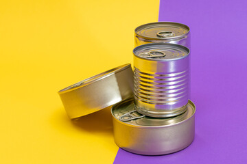 A Group of Stacked Tin Cans with Blank Edges on Split Yellow and Violet Background. Canned Food. Different Aluminum Cans for Safe and Long Term Storage of Food. Steel Sealed Food Storage Containers