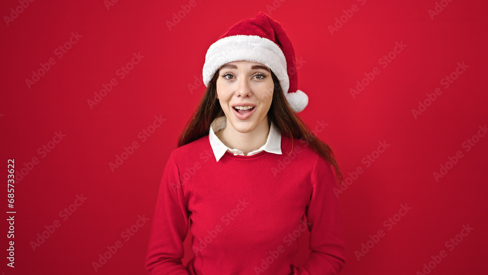 Sticker Young hispanic woman wearing christmas hat with surprise expression over isolated red background