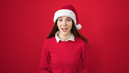 Young hispanic woman wearing christmas hat with surprise expression over isolated red background