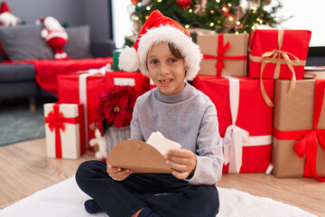 Obraz na płótnie Canvas Adorable hispanic boy putting santa claus letter in envelope sitting by christmas tree at home