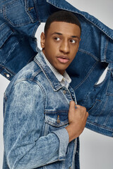 young trendy african american man in stylish denim outfit posing on white backdrop, fashion