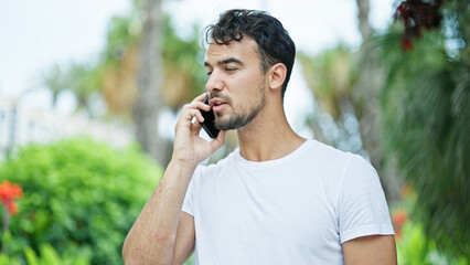 Young hispanic man talking on smartphone with serious expression at park