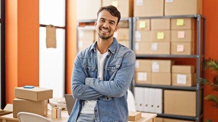 Young hispanic man ecommerce business worker standing with arms crossed gesture at office