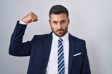 Handsome hispanic man wearing suit and tie strong person showing arm muscle, confident and proud of power