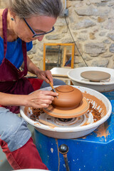 A woman polishing a piece of clay on the potter's wheel with a special tool.