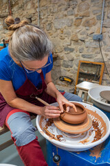 A woman putting the finishing touches to a piece of pottery on the potter's wheel.
